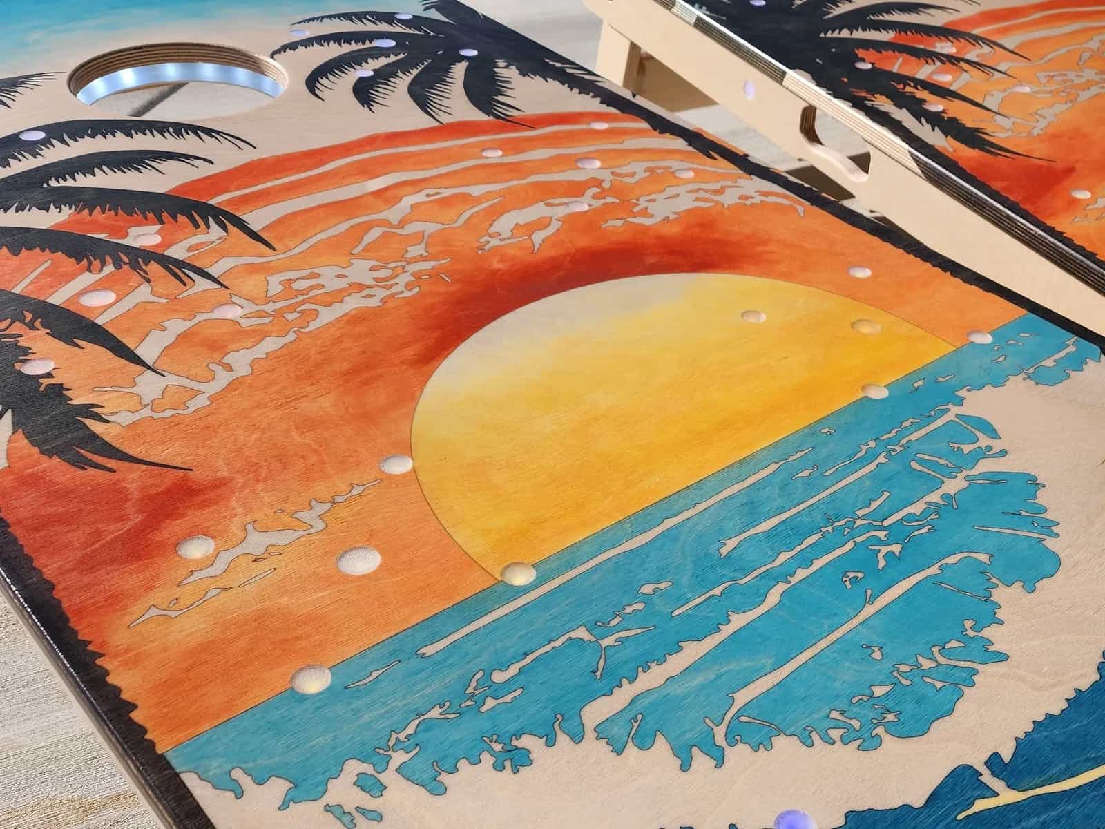 Close-up of a YoreBoard cornhole board with a hand-stained beach sunset scene and integrated LED scoring.
