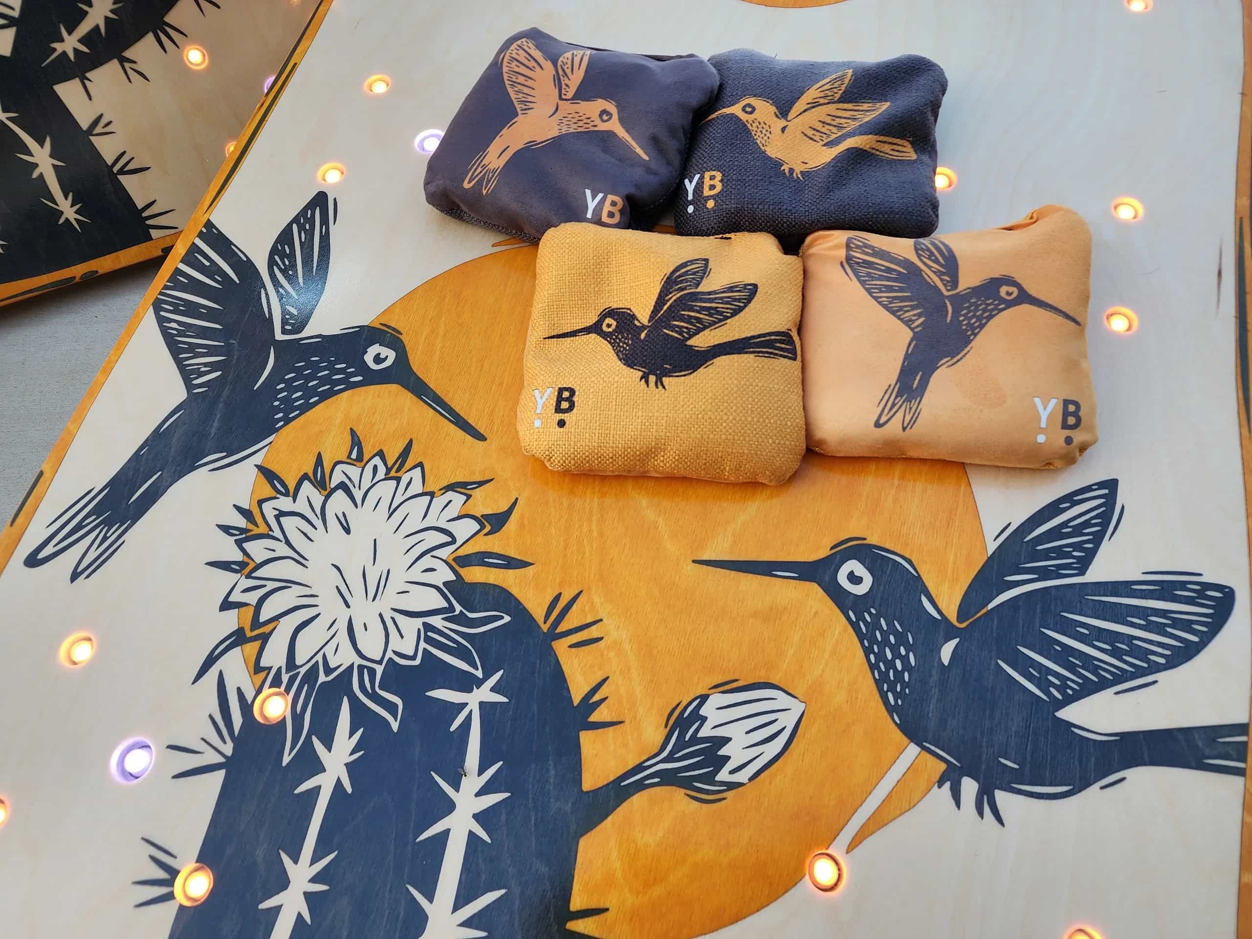 Detailed shot of a YoreBoard cornhole board highlighting its custom hand-stained desert-themed artwork with hummingbirds and cacti.