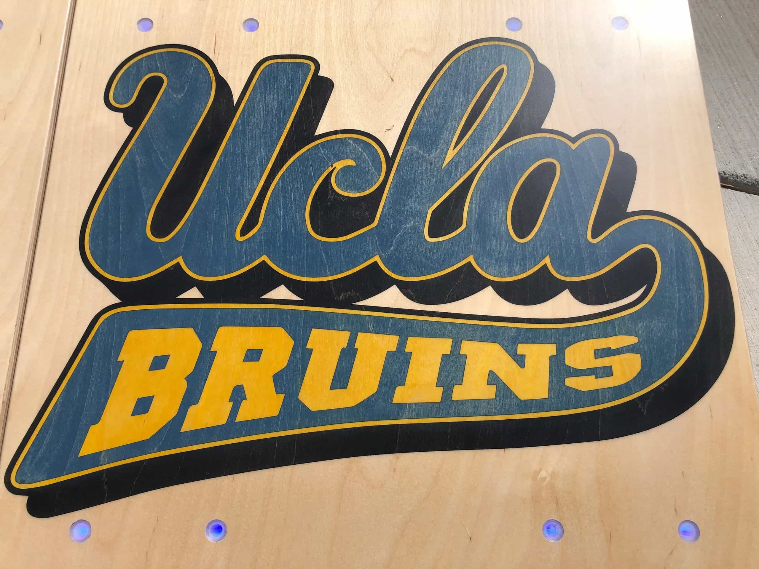 Close-up of a YoreBoard cornhole board with a hand-stained UCLA Bruins logo and integrated LED scoring.