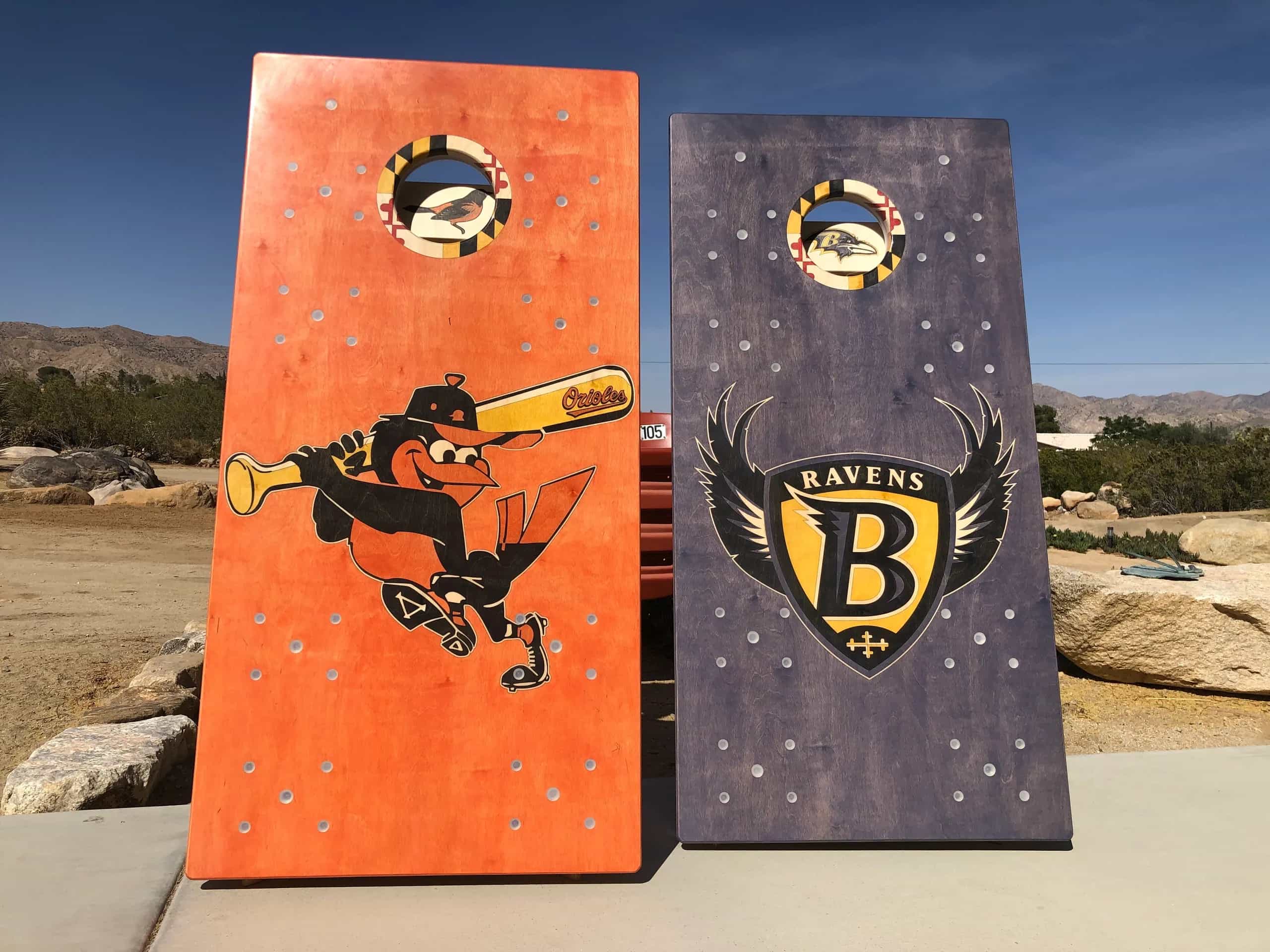 A pair of YoreBoard cornhole boards showcasing detailed hand-stained Baltimore Orioles and Ravens team graphics, designed for sports fans.