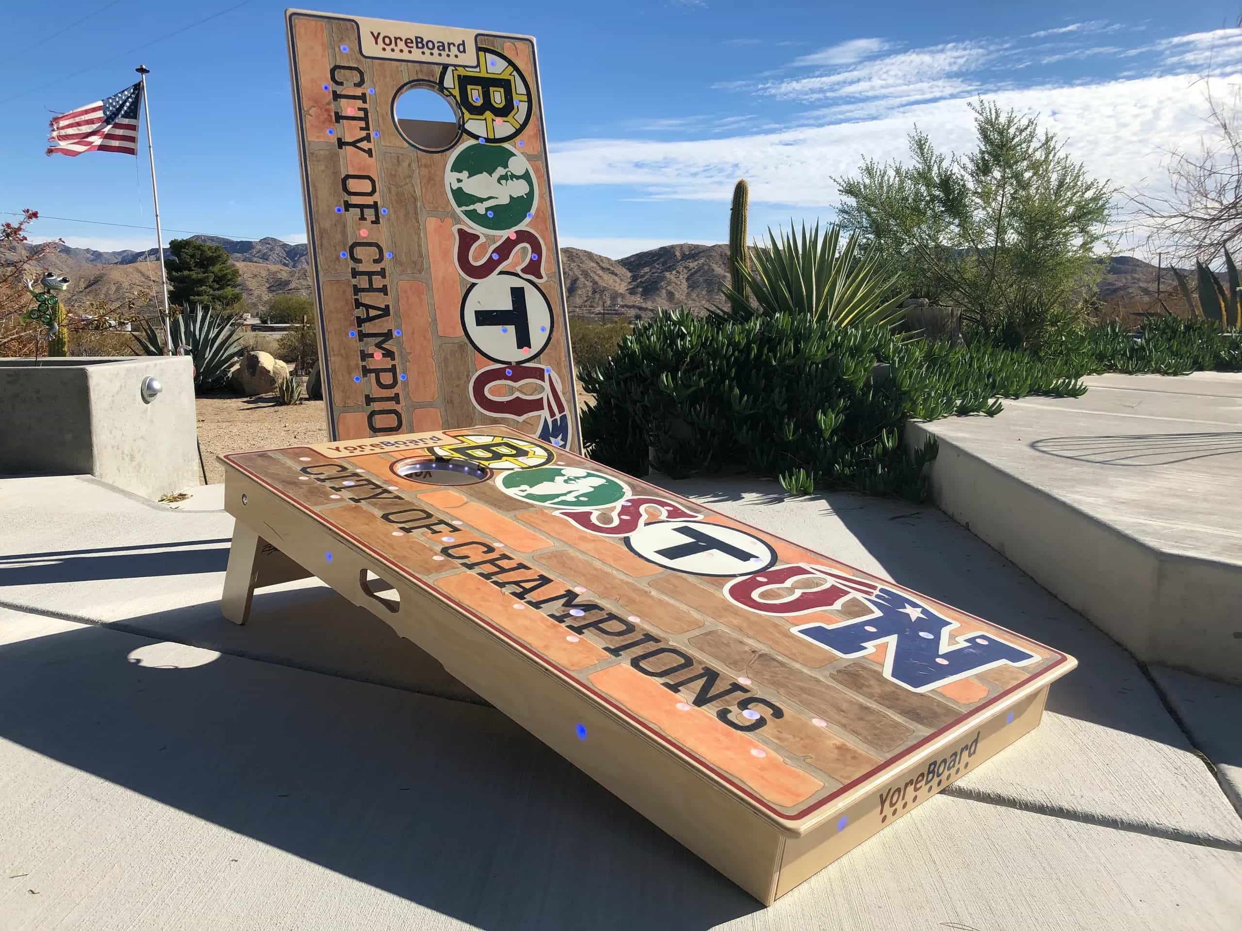 A pair of YoreBoard cornhole boards showcasing detailed hand-stained designs celebrating Boston as the 'City of Champions,' with a weathered brick aesthetic.