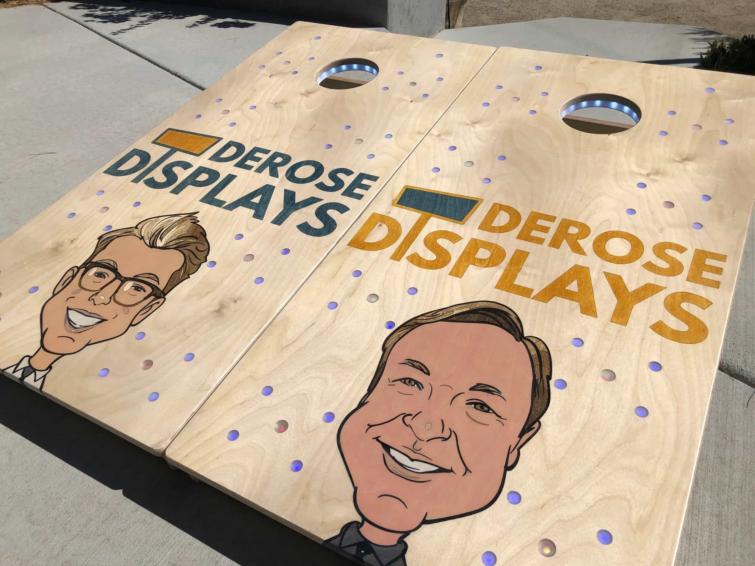 A pair of YoreBoard cornhole boards showcasing personalized, hand-stained company branding and unique caricature artwork, designed for promotional events or office use.