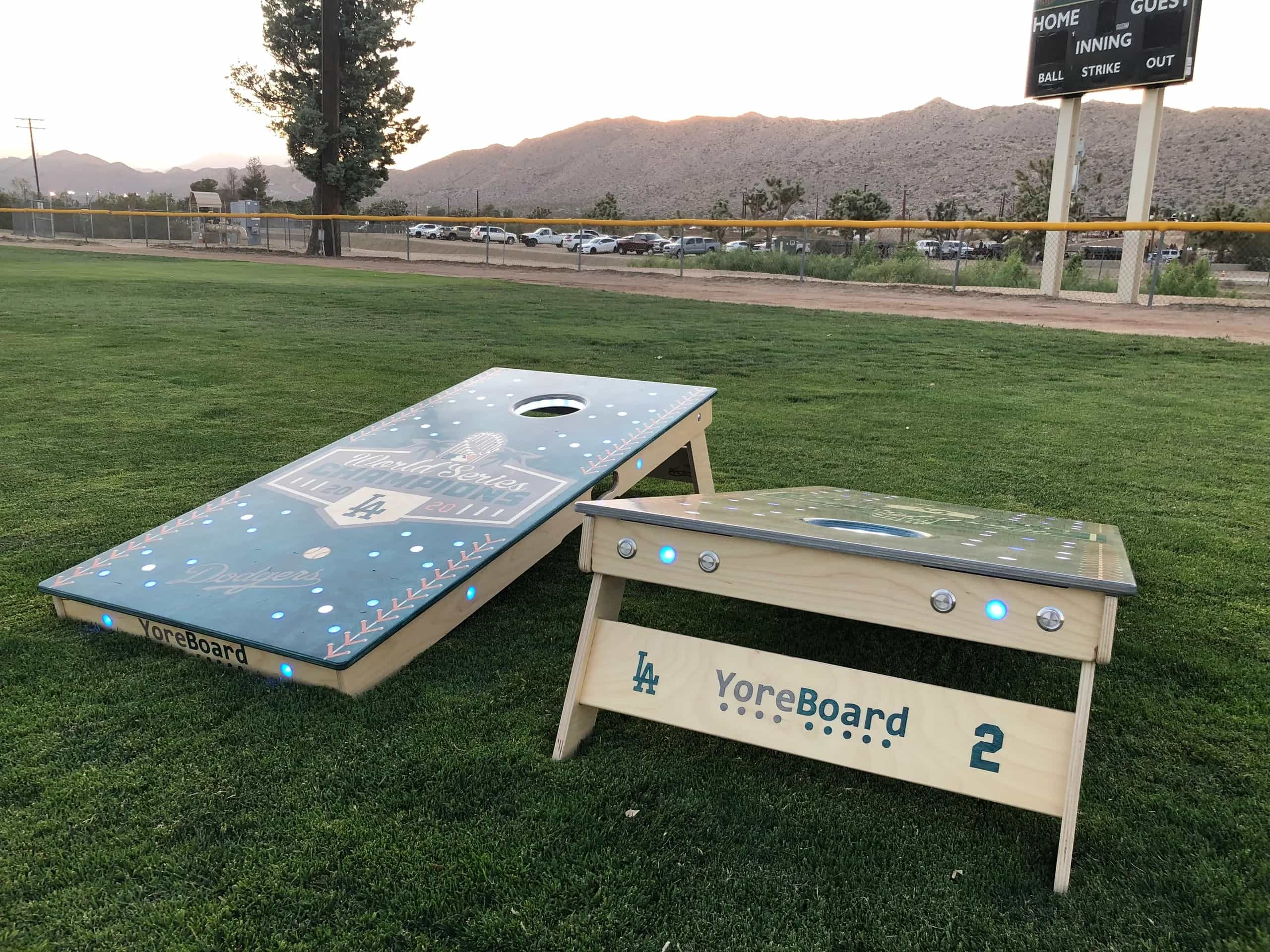 Custom Los Angeles Dodgers YoreBoard cornhole set with team branding and blue and white Scoring LEDs on a baseball field.