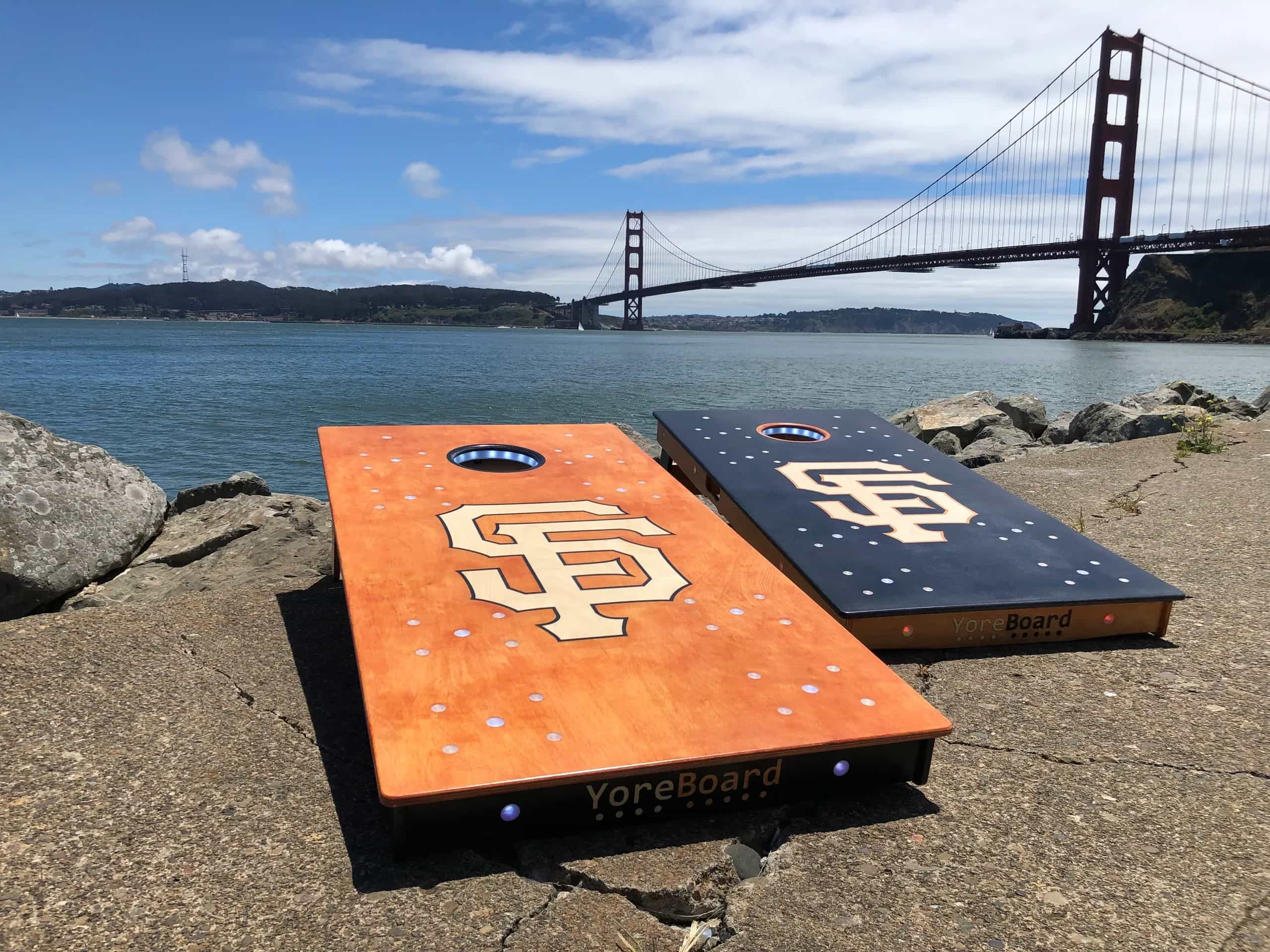 A pair of YoreBoard cornhole boards showcasing detailed hand-stained San Francisco Giants baseball team graphics, set in a scenic bay area location with the iconic Golden Gate Bridge.