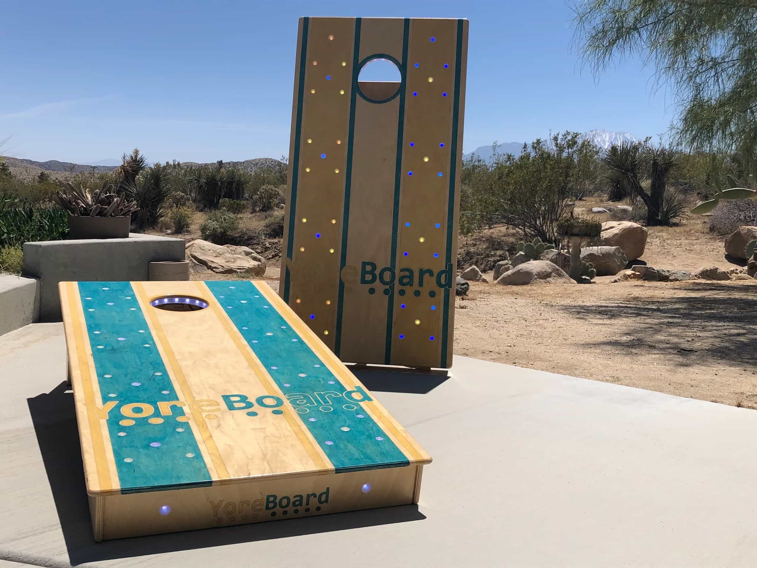 A pair of YoreBoard cornhole boards showcasing their brand's distinctive hand-stained design with teal accents and integrated LED scoring, ready for outdoor play.