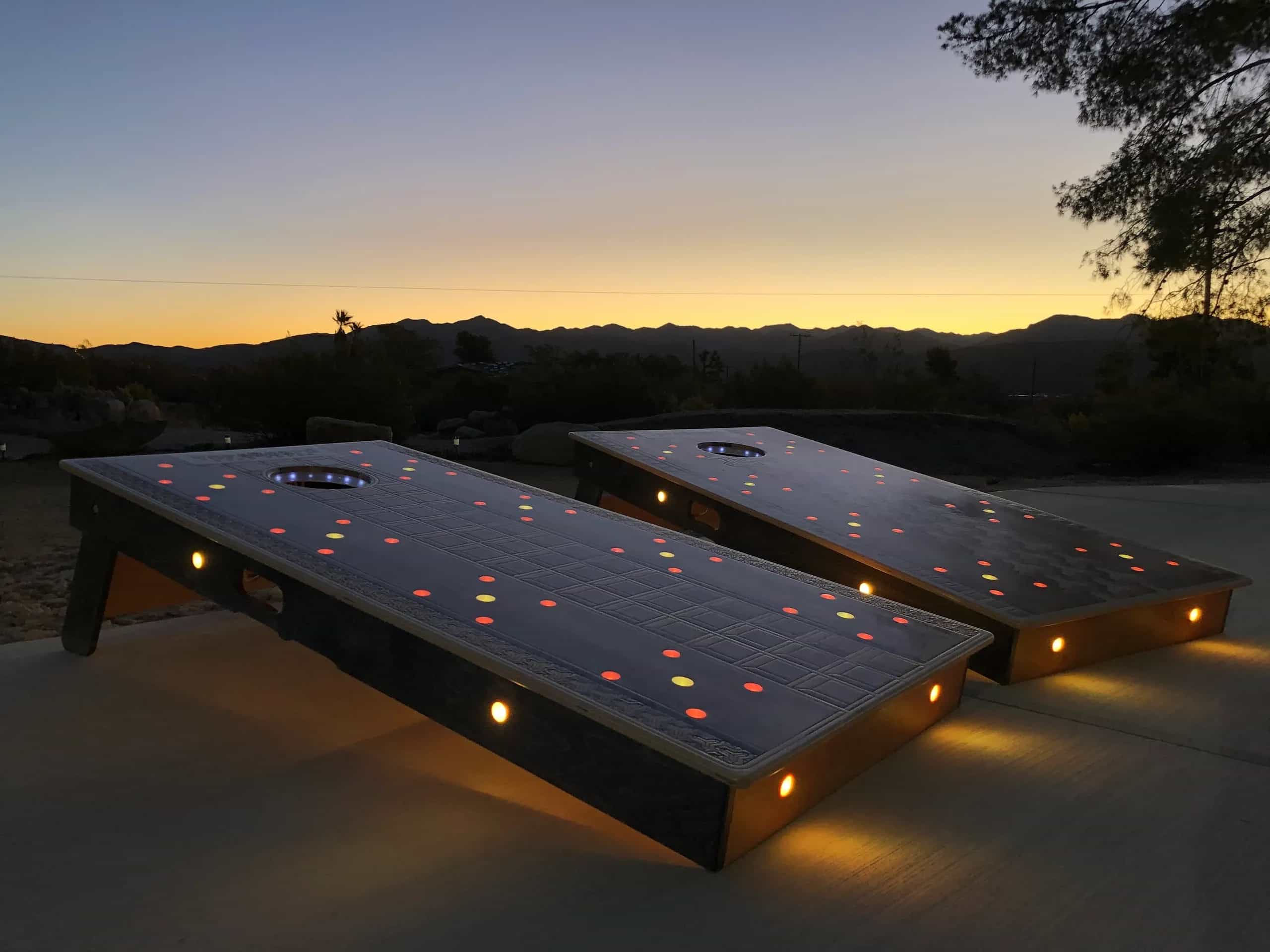 YoreBoard cornhole set lit up with colorful red and yellow LEDs, perfect for evening games, with a scenic sunset backdrop.