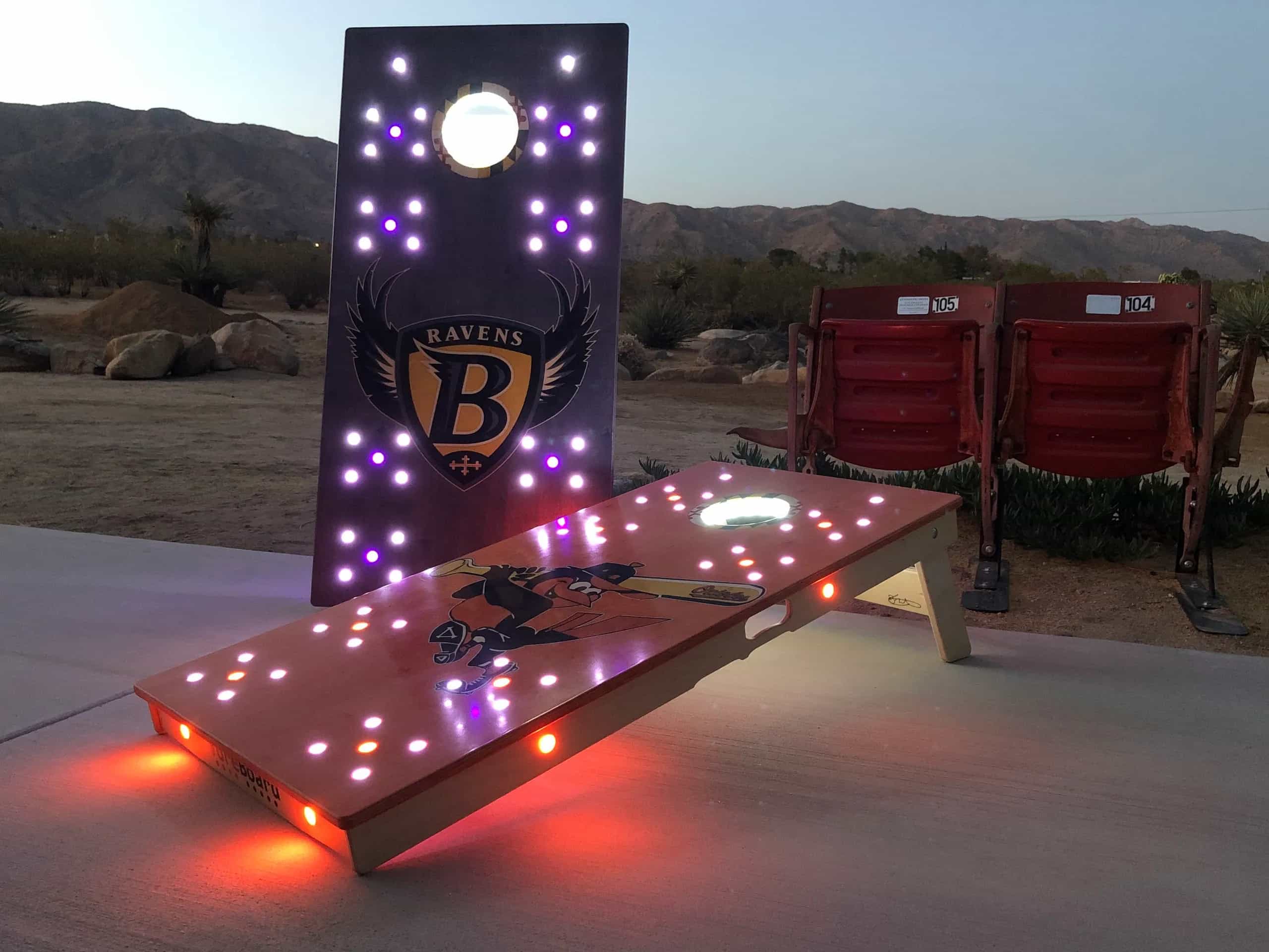 Personalized YoreBoard cornhole boards with Baltimore Ravens and Orioles branding, illuminated by multi-colored Scoring LEDs for ultimate fan engagement.