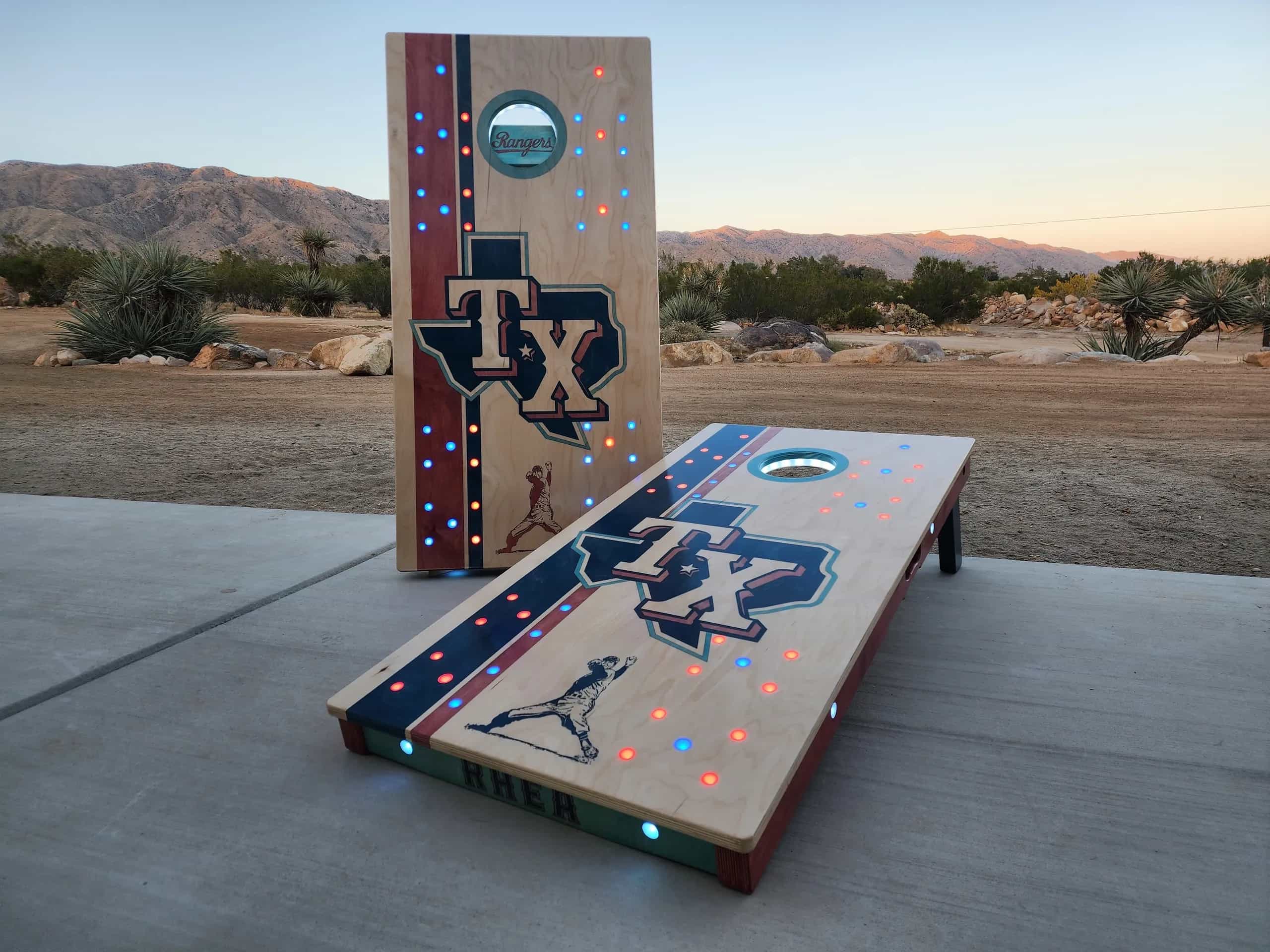 Detailed view of a personalized YoreBoard cornhole board showcasing 'Rangers' text through the hole, vibrant team-colored stripes, and integrated red and blue Scoring LEDs.