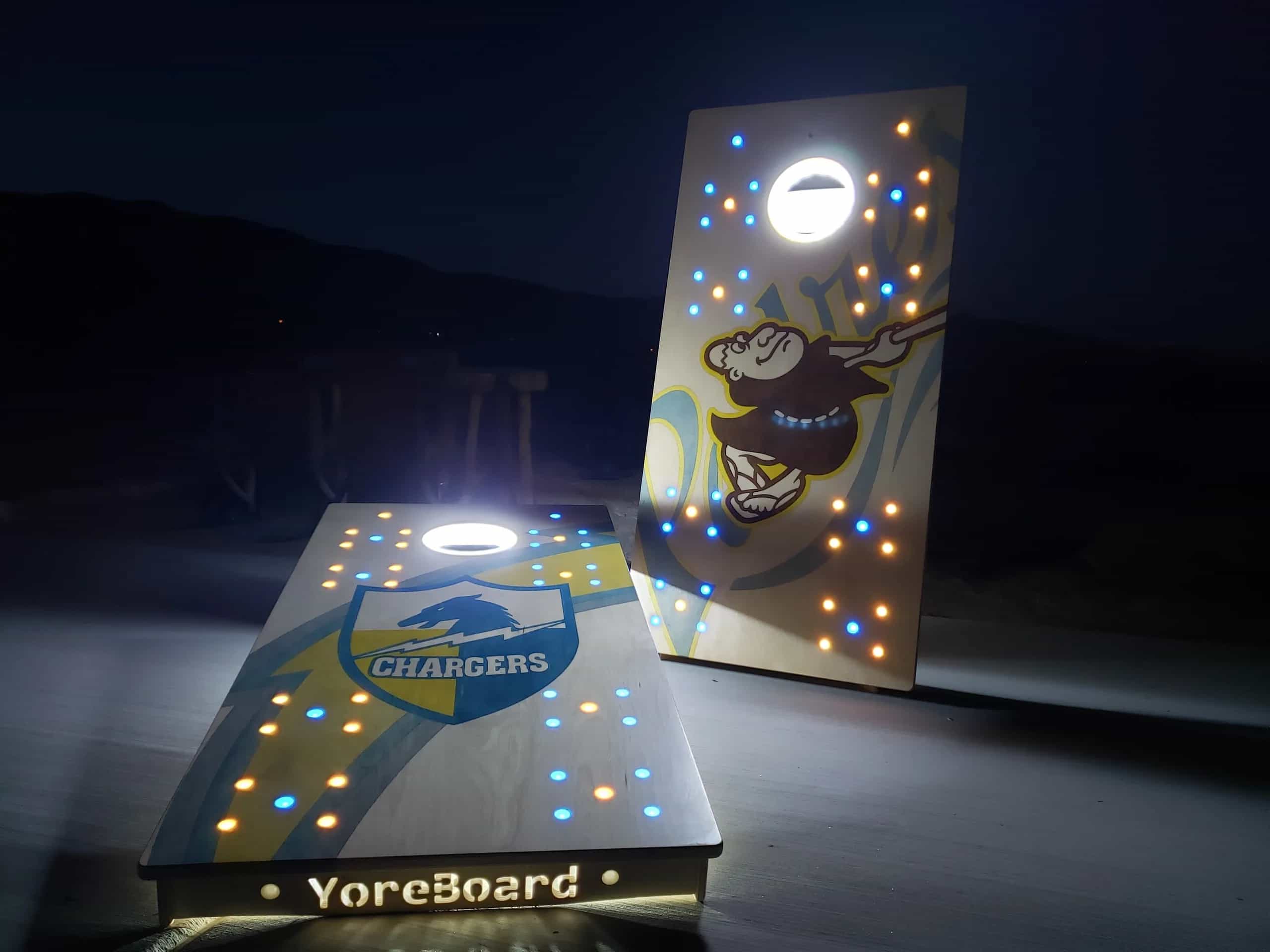 Personalized YoreBoard cornhole boards celebrating San Diego sports, featuring Chargers and Padres mascots, and integrated yellow and blue Scoring LEDs for evening play.