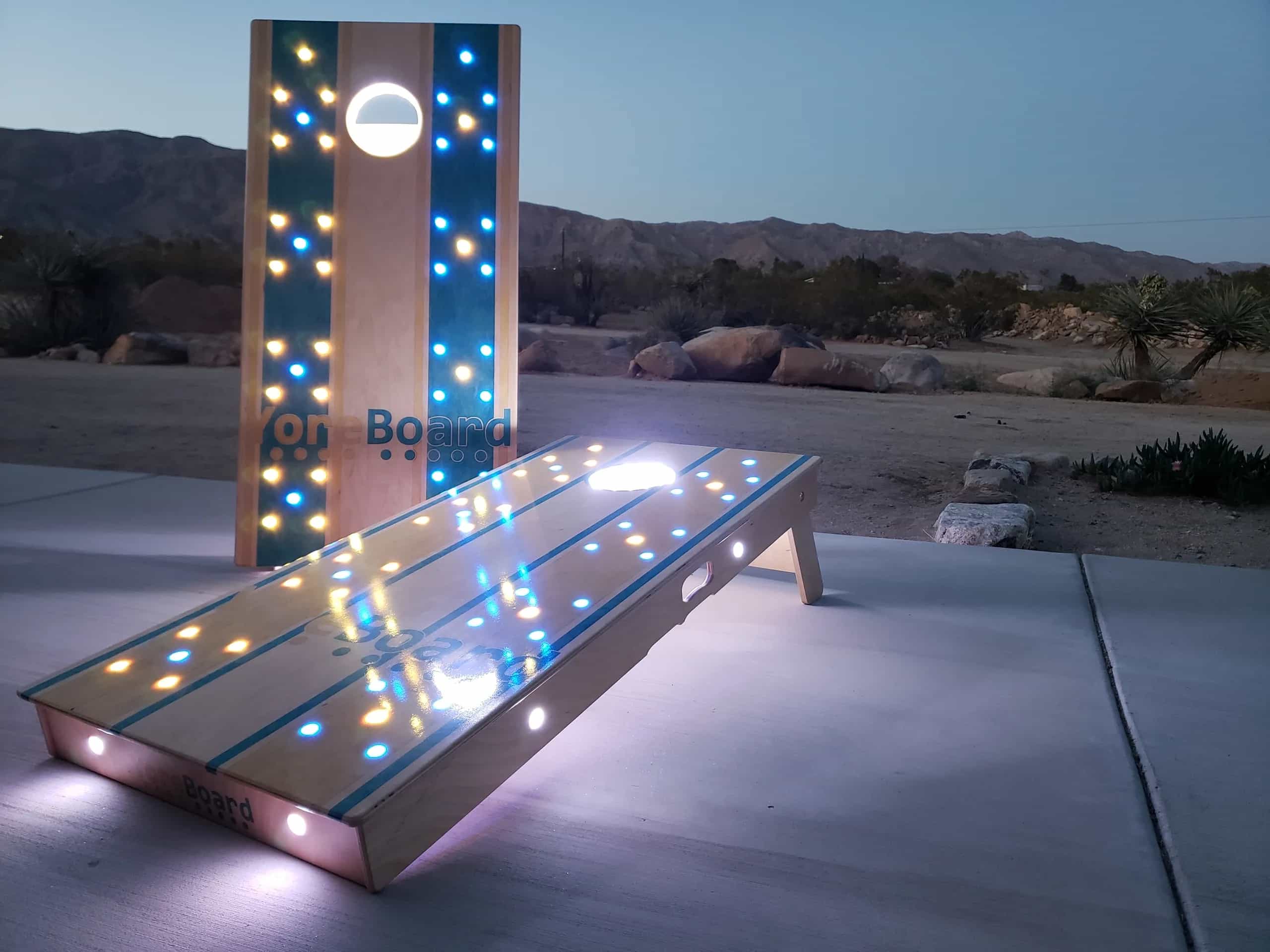Illuminated standard YoreBoard cornhole set with LED lights and stainless steel buttons at dusk.