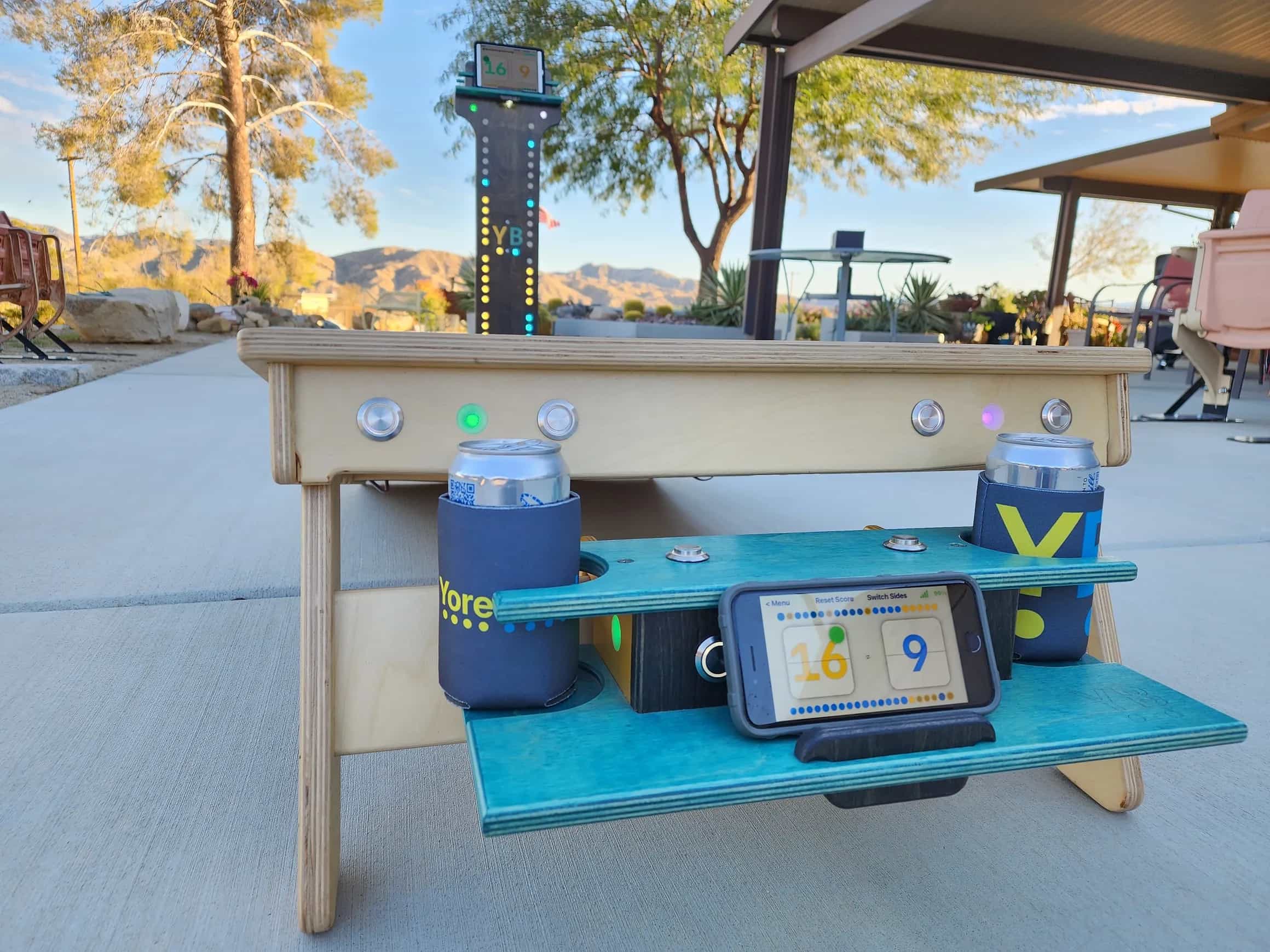 Comprehensive YoreBoard cornhole display showing a multi-colored LED score tower and a cornhole board equipped with an integrated scorebox for real-time digital scoring and drink storage.