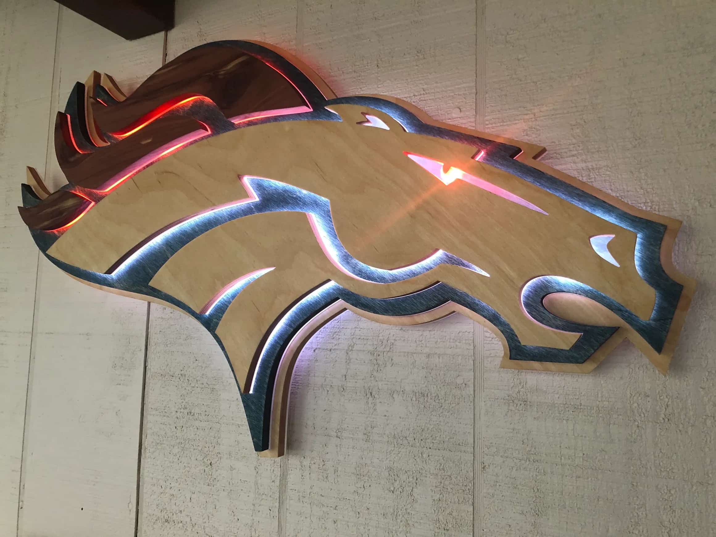 Illuminated Denver Broncos emblem crafted from multiple layers of wood, with LED lights highlighting the outlines of the horse's mane and face, creating a striking visual effect.