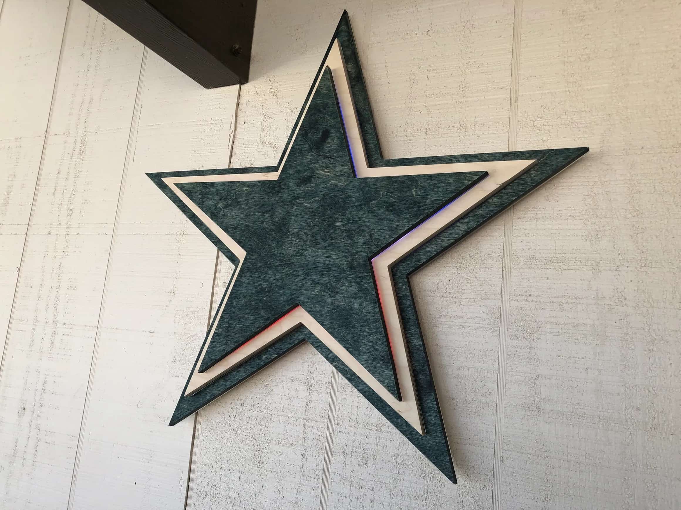 Custom-made, multi-layered Dallas Cowboys star emblem crafted from wood, showcasing the iconic star shape with a deep blue-green primary color and contrasting light wood accents, creating a dimensional effect.