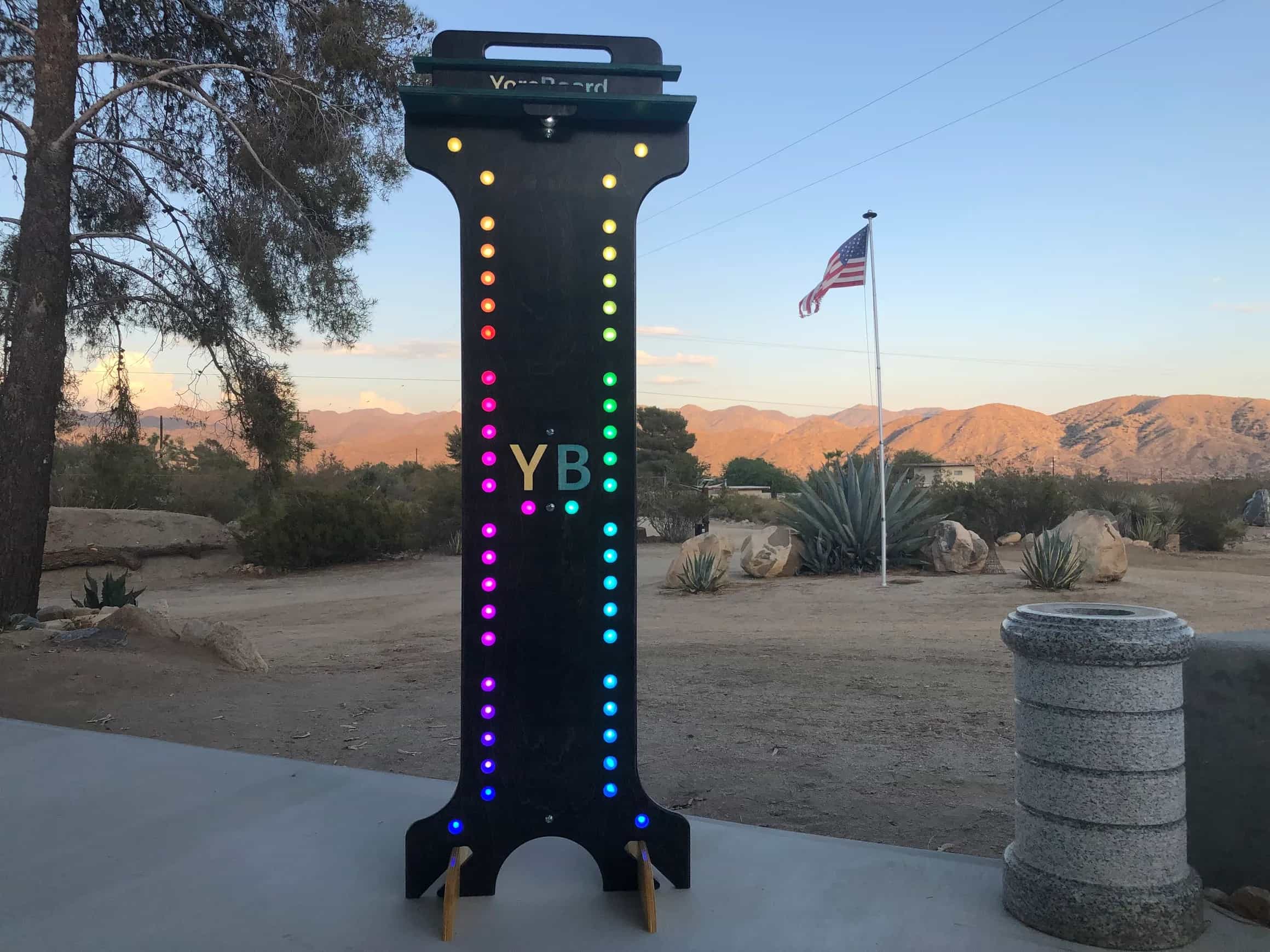 YoreBoard score tower illuminated with vibrant multi-colored Scoring LEDs, featuring the 'YB' logo, set outdoors at dusk.