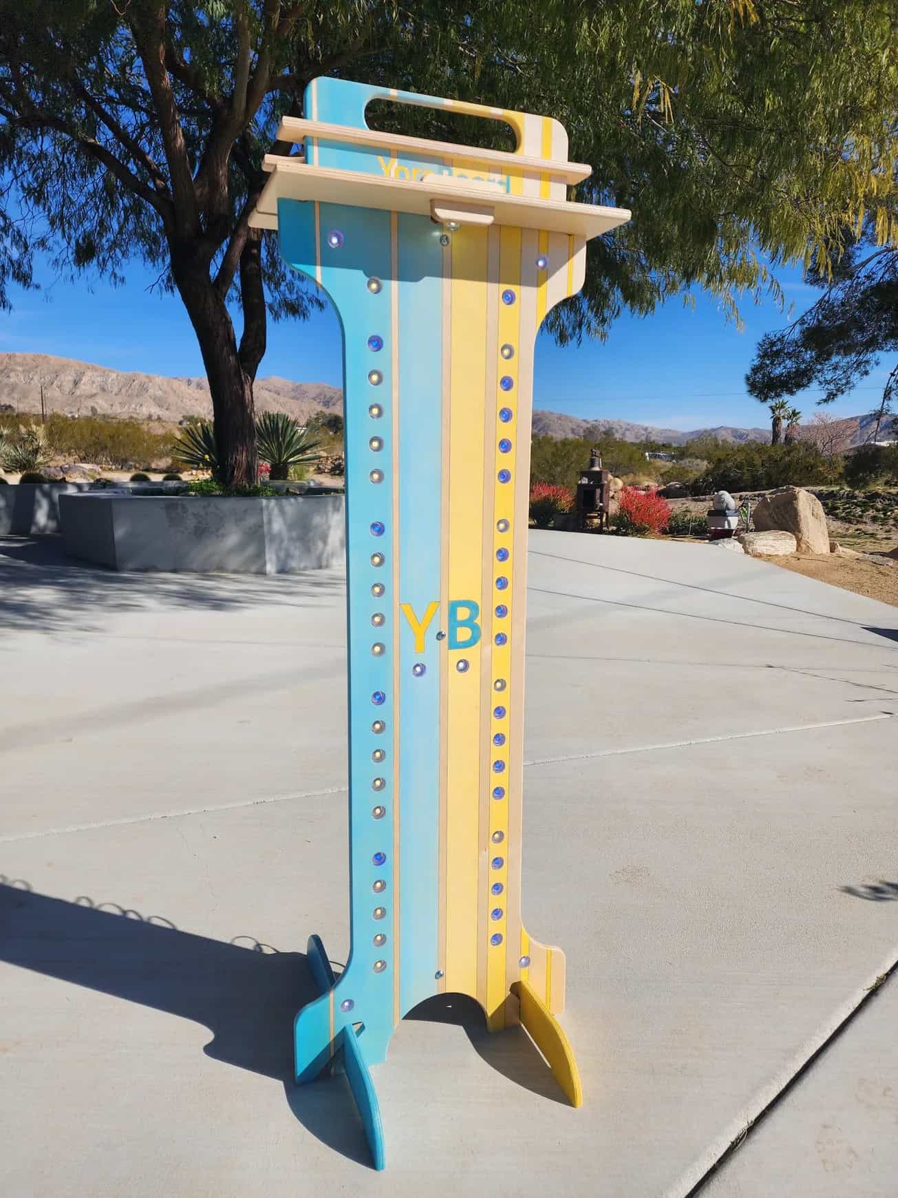 YoreBoard score tower with blue and yellow striped design and visible unlit Scoring LED holes, ready to display scores, set outdoors in daylight.